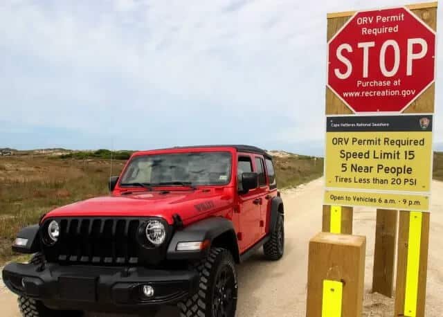 OBX RV Jeep Rental: Beach-Ready 4Γ4 for the Week 1 Red Jeep Wrangler from Beach4x4 parked at the Cape Hatteras National Seashore ORV beach access ramp, beside the ORV permit and 20 PSI tire pressure sign.