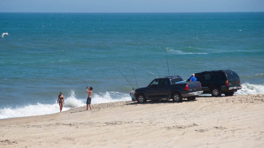 Two people stand at the surf line beside four-wheel-drive vehicles parked on the sand at Cape Hatteras National Seashore.