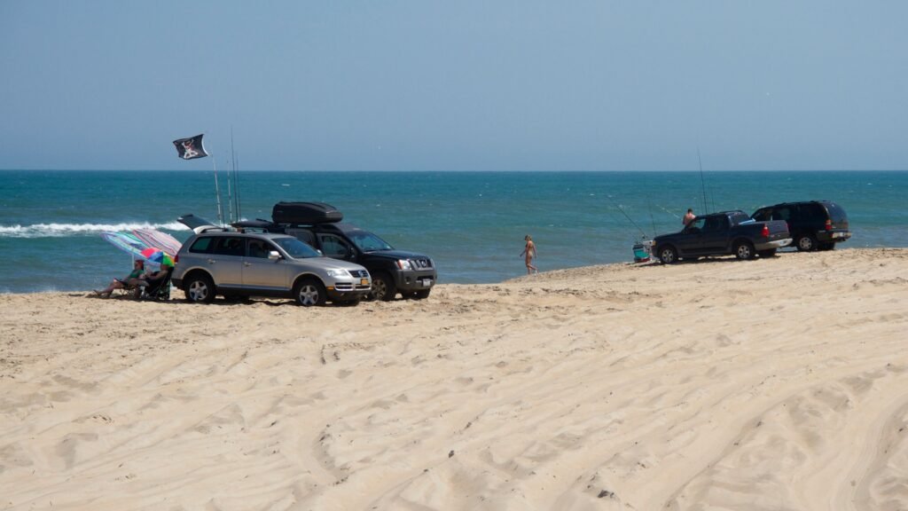 Four-wheel-drive vehicles spread along the wide sand at Cape Point with the ocean beyond.