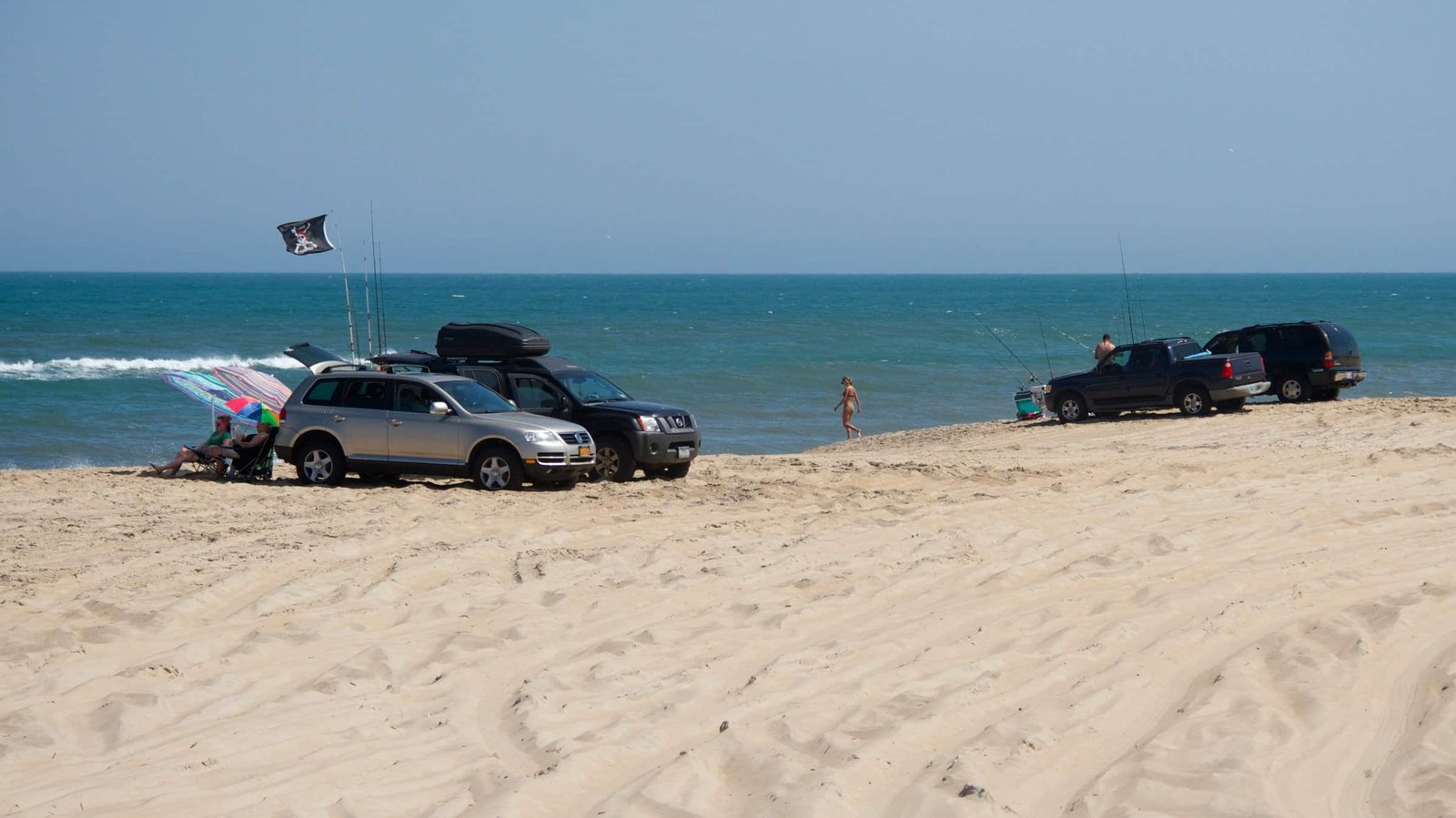 Four-wheel-drive vehicles spread along the wide sand at Cape Point with the ocean beyond.