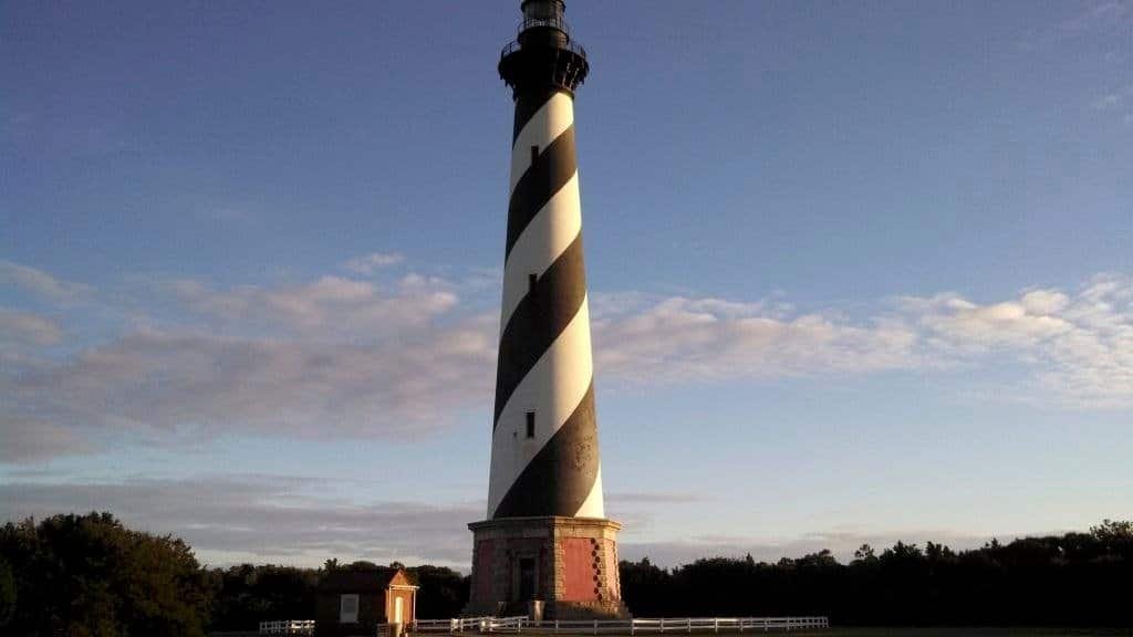 The black-and-white spiral-striped Cape Hatteras Lighthouse lit by low autumn sunlight against a blue sky.