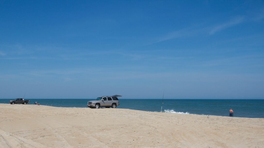 Four-wheel-drive vehicles parked in a line on the open sand at Cape Hatteras National Seashore under a deep blue sky.