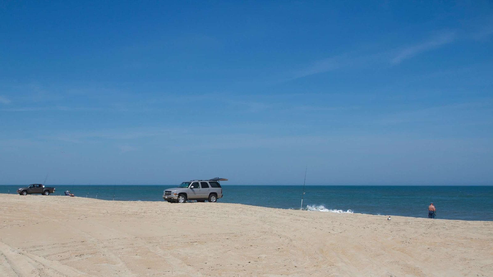 Four-wheel-drive vehicles parked in a line on the open sand at Cape Hatteras National Seashore under a deep blue sky.