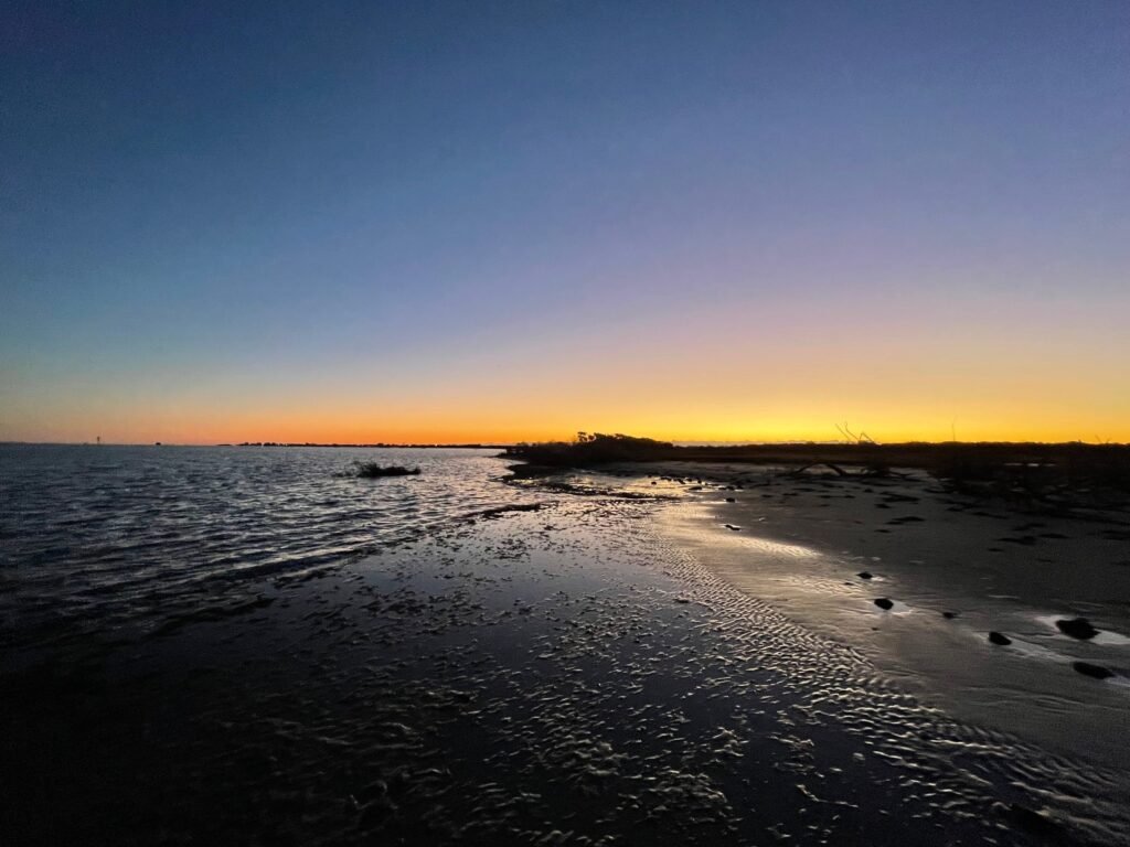 Low sun over the shallow sound shore near Hatteras with a dark shoreline in the distance.
