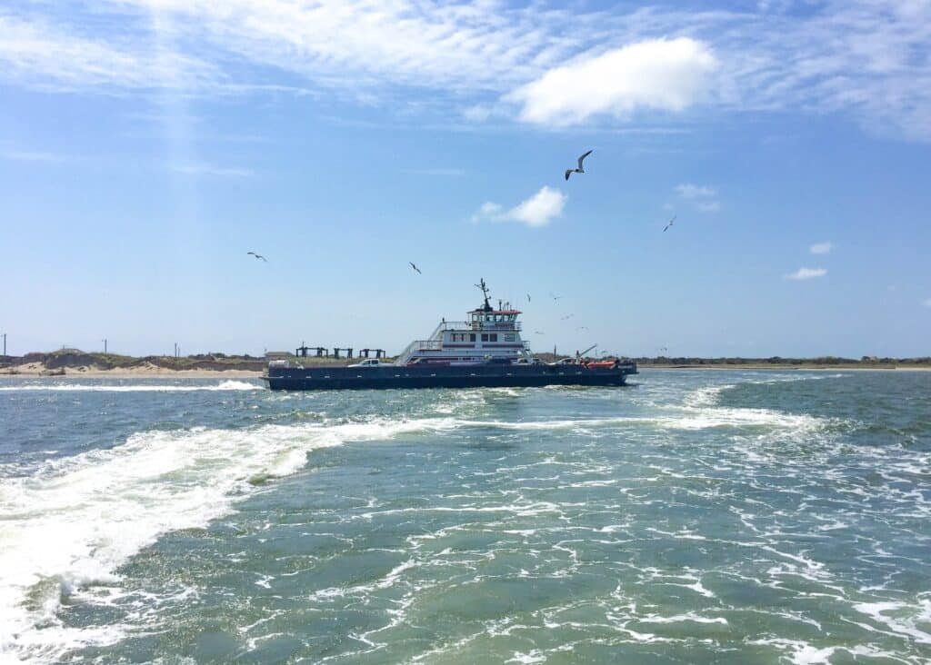 A state ferry crossing the inlet toward Ocracoke Island, seen from the wake of another vessel.