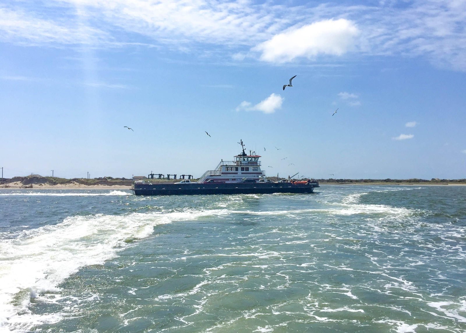 A state ferry crossing the inlet toward Ocracoke Island, seen from the wake of another vessel.