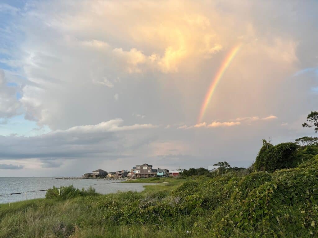 A rainbow arcs over the rooftops and trees of Ocracoke Village at sunset.