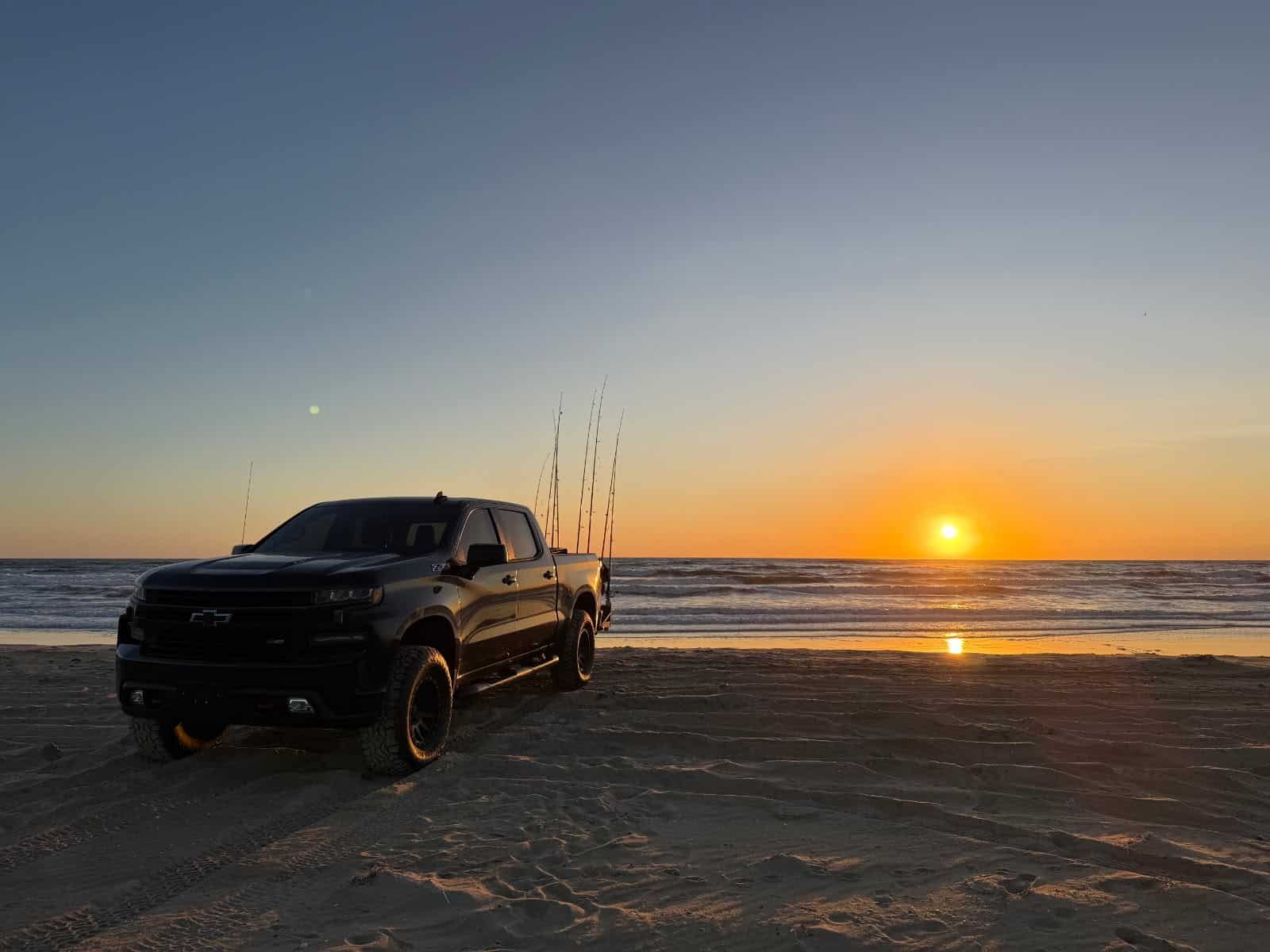 Chevy Silverado 4x4 rental parked at sunrise on the Outer Banks beach with surf rods set
