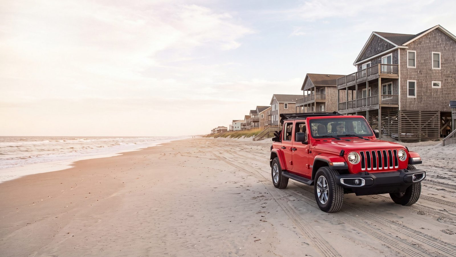 A red Jeep Wrangler parked on the sand below a row of oceanfront beach houses on pilings at sunset — Carova, Outer Banks NC